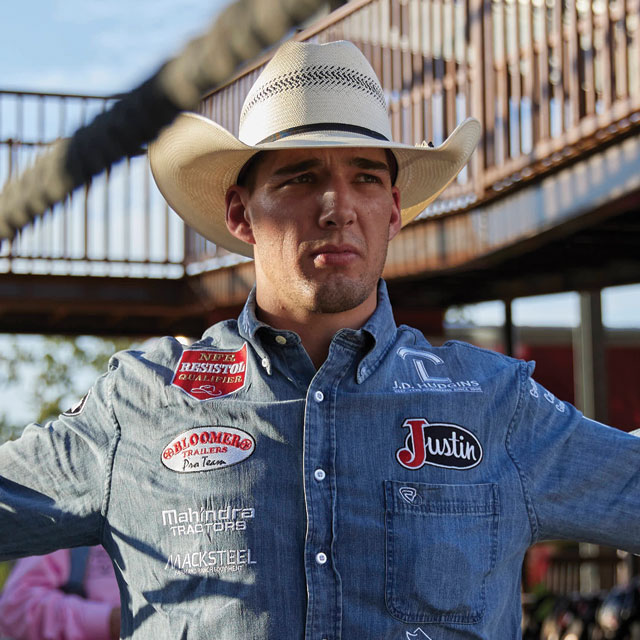 Jess Pope wearing a denim shirt and cowboy h at using ropes to stretch before riding.